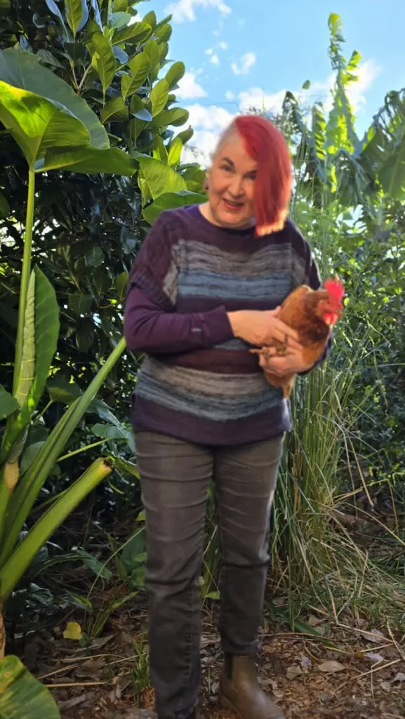 Anne walks through lush garden with brown chicken under her arm
