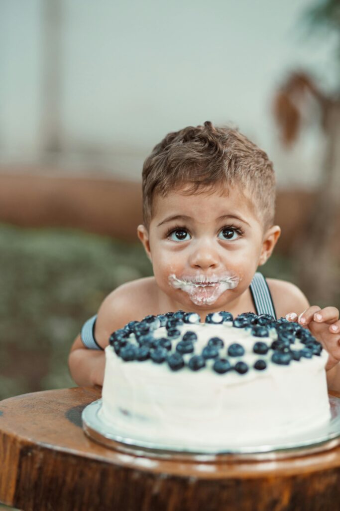 Cute child with cake and blueberries at a birthday celebration.